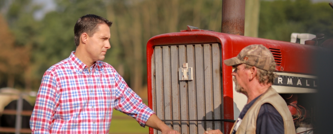 Frank LaRose standing by a red tractor talking with a farmer